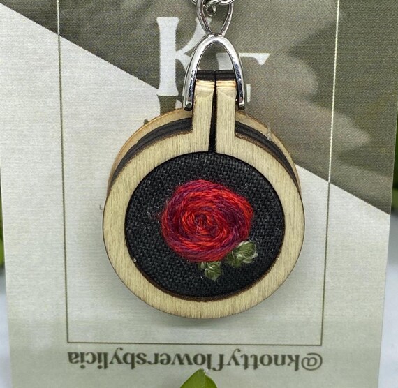 hand stitched Red woven rose with multiple shades of light, medium, and dark red around and two small green leaves on a black background.
