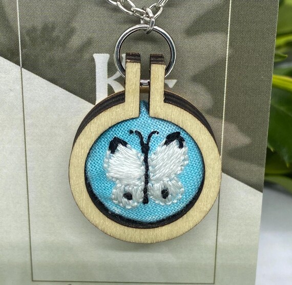 hand stitched embroidered White butterfly with black on the tips of each top wing, and one black spot on each bottom wing, it is on a sky blue background fabric