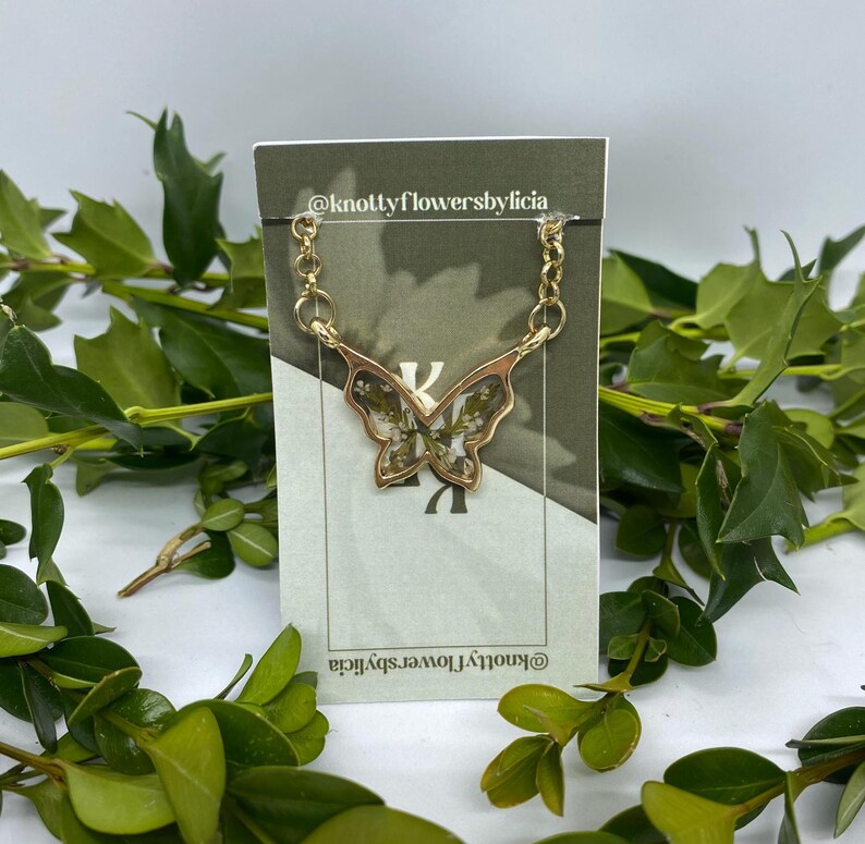 handmade resin butterfly shaped pendant delicate tiny green leaves with very very small white flowers scattered on top.