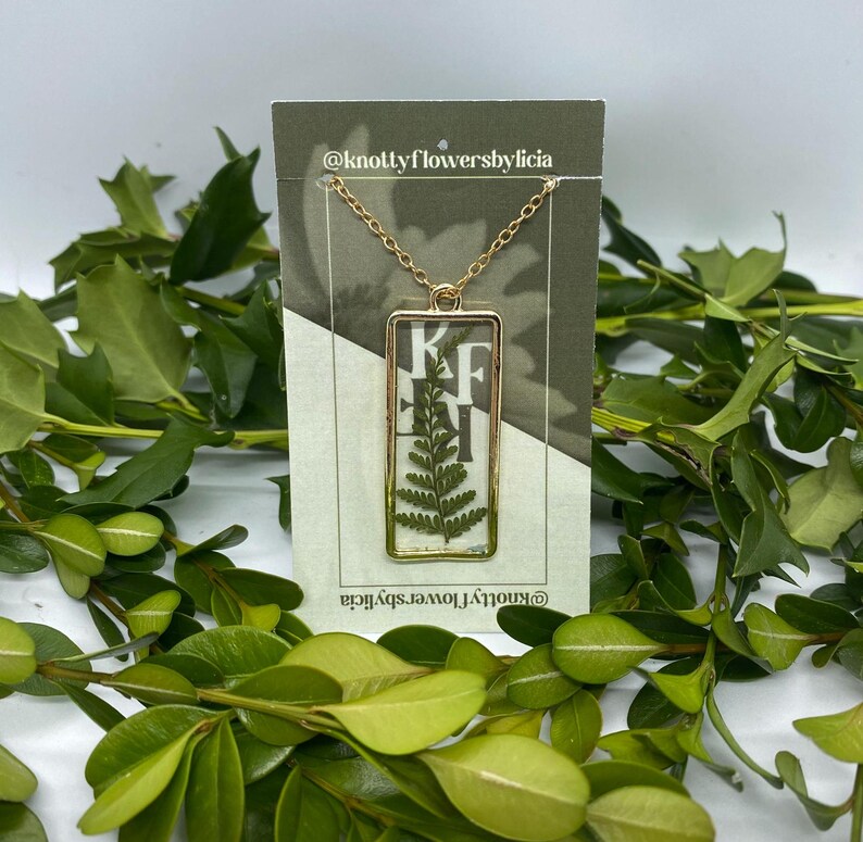 handmade resin necklace with a fern leaf as the centerpiece of the gold rectangle shaped pendant