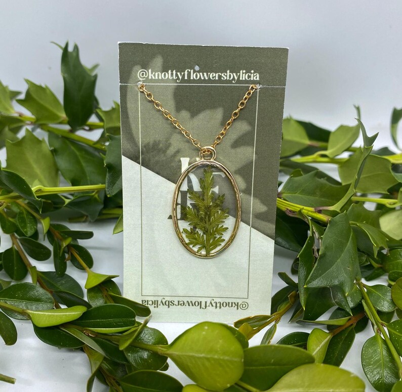 handmade resin necklace with a fern leaf as the centerpiece of the gold oval shaped pendant